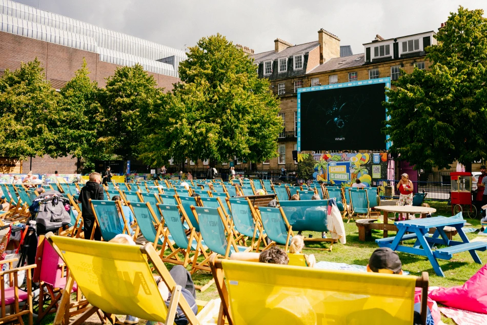 People sat on a temporary grassed area watching a movie on a big cinema screen