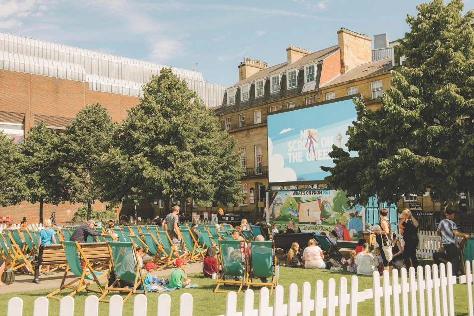 People sat on a temporary grassed area watching a movie on a big cinema screen