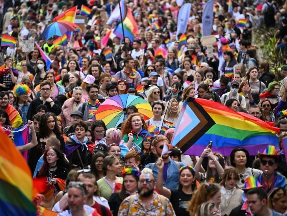 A crowd of people celebrating pride with numerous rainbow flags and outfits